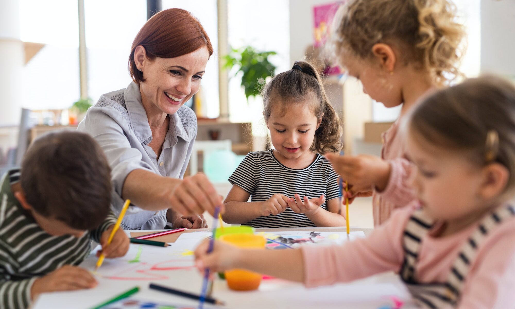 Group of small nursery school children with teacher indoors in classroom, painting