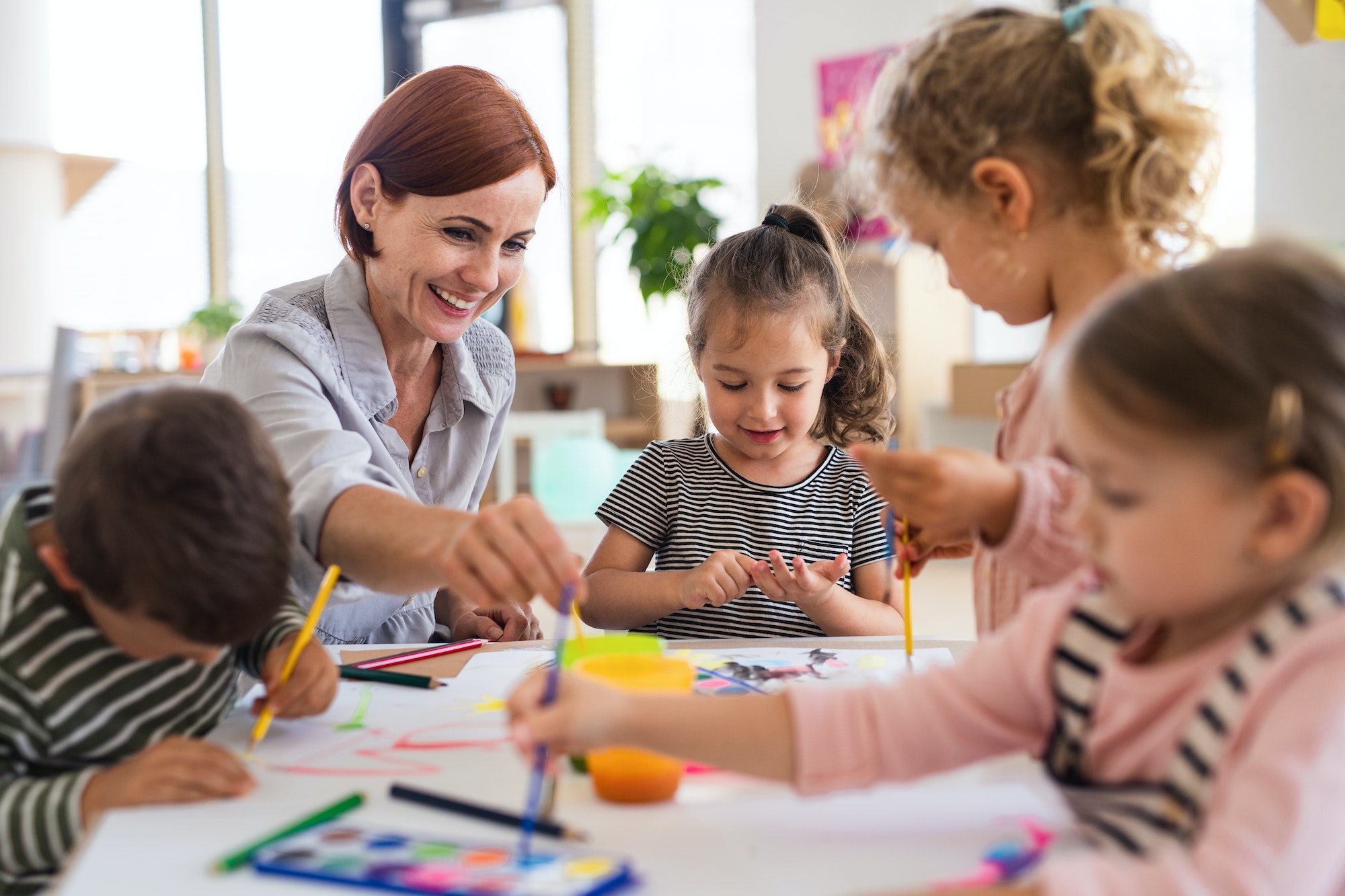 Group of small nursery school children with teacher indoors in classroom, painting